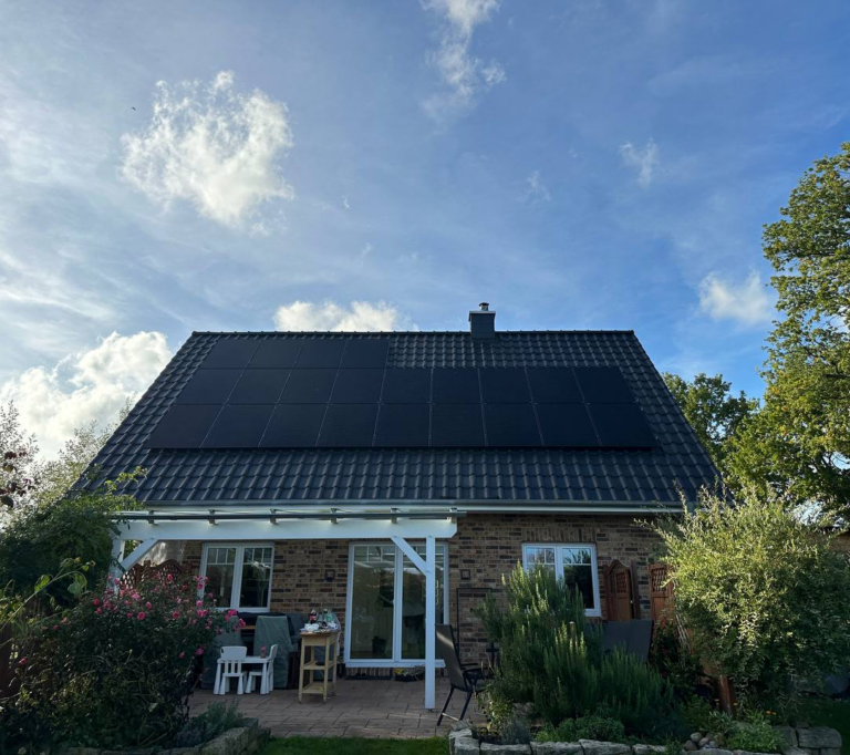 Ein Haus mit Solaranlagen auf dem Dach unter einem strahlend blauen Himmel. Im Vordergrund sind Gartenmöbel zu sehen.