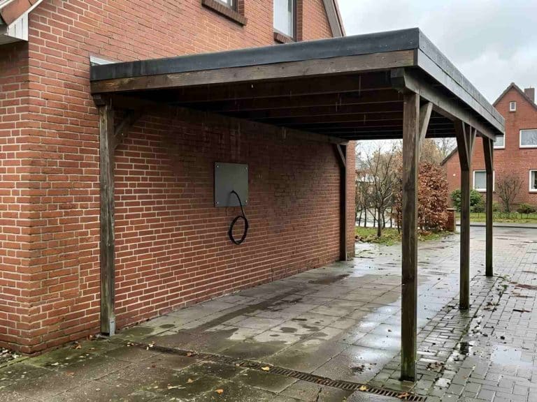 Leere Montageplatte und eine abgedeckte Leitung an der Backsteinwand eines Carports an einem grauen Regentag