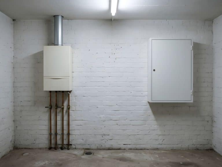 Älterer Gas-Wandkessel im Keller neben einem neuen weißen Zählerschrank