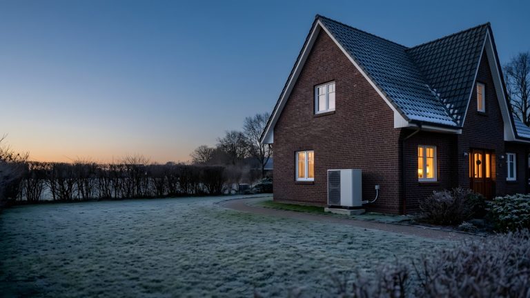 Luft-Wasser-Wärmepumpe neben einem norddeutschen Klinkerhaus an einem frostigen Winterabend mit erleuchteten Fenstern