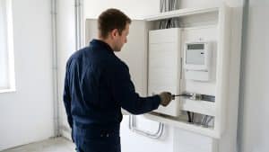 Elektriker prüft die Verdrahtung in einem modernen Zählerschrank mit digitalem Stromzähler und Leitungsschutzschaltern
