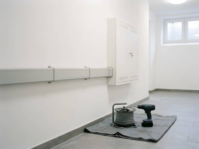Neu montierter Kabelkanal an einer weißen Wand führt zu einem geschlossenen Zählerschrank, davor Kabeltrommel und Akkuschrauber auf einer Abdeckplane